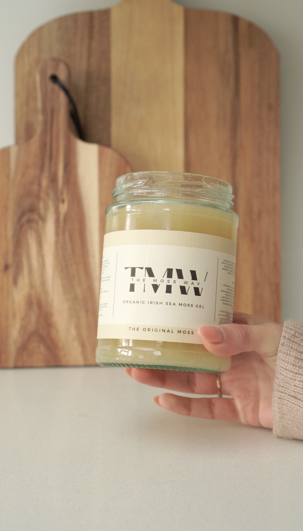 A hand holding The Original Moss 500ml jar against a wooden board
